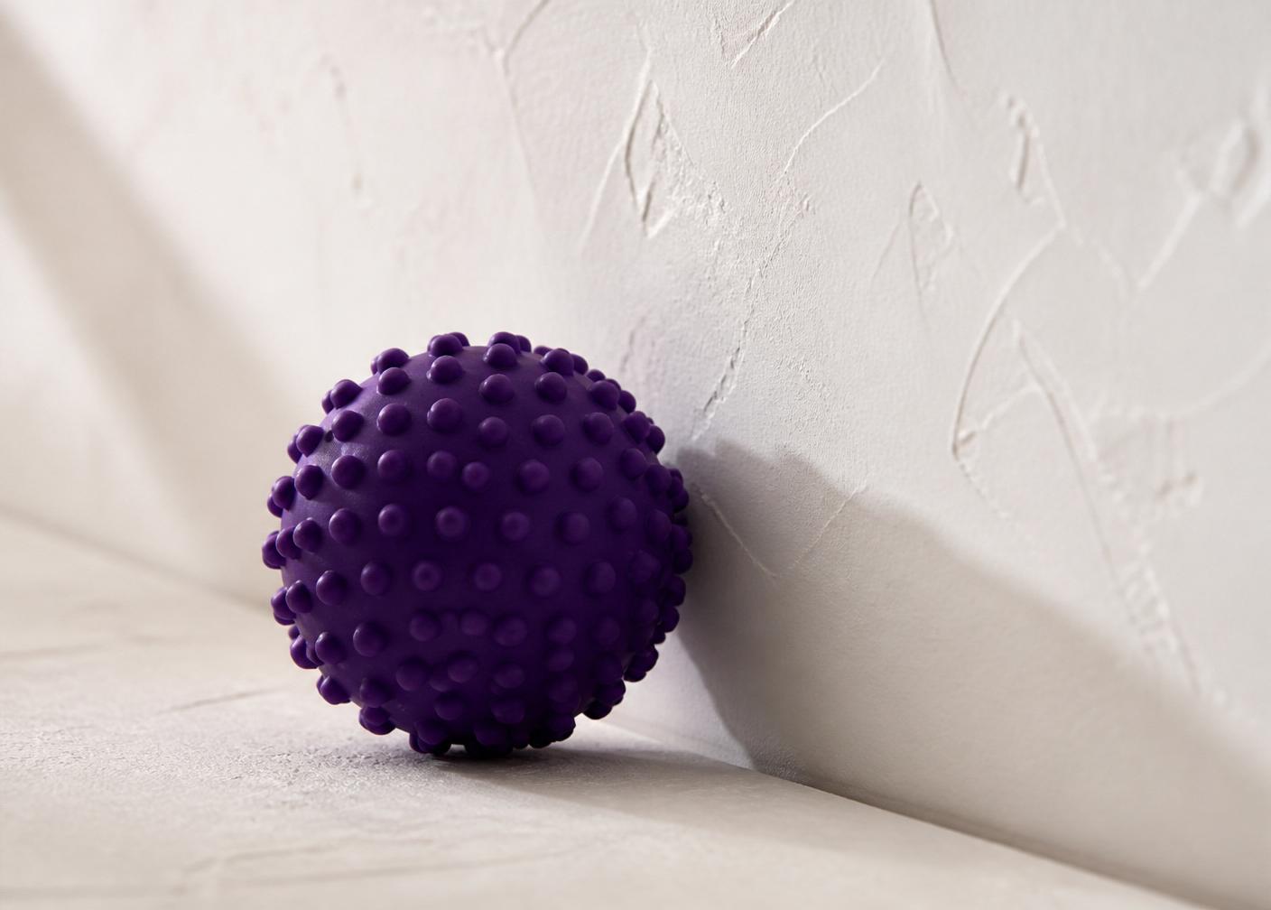 A small purple massage ball resting against a plain white wall